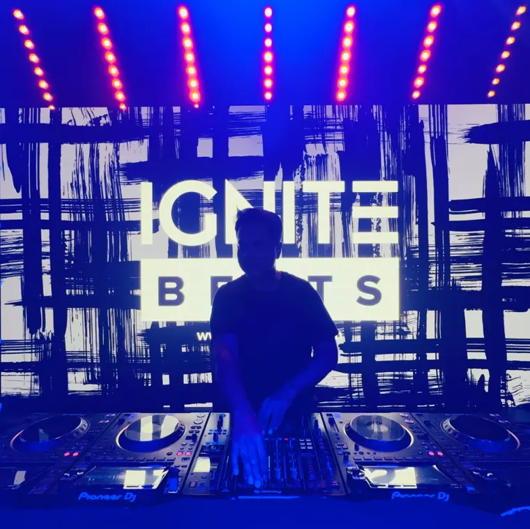 IGNITE Beats mixing on four Pioneer DJ players and a club mixer, the IGNITE Beats logo lit on the screen behind him